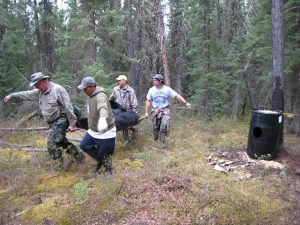 4 men carry a black bear out of the woods